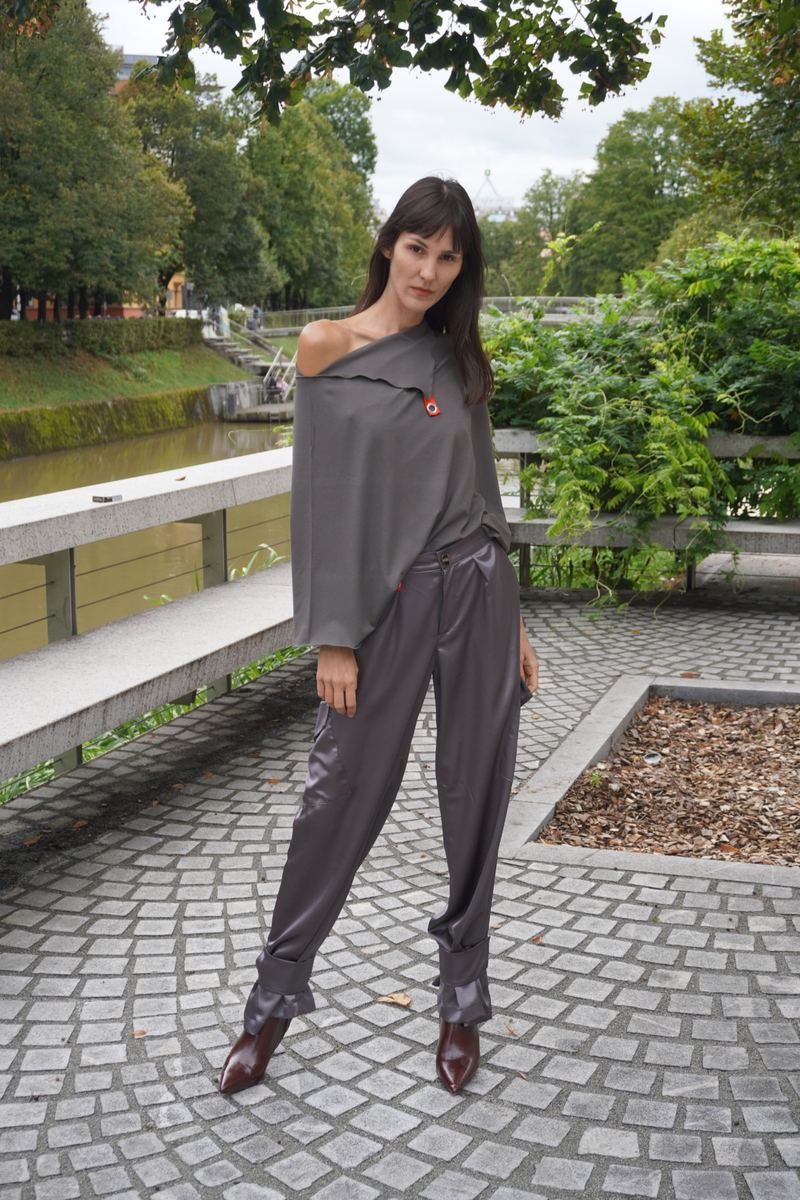 Modelka v sivi asimetrični majici in satenastih hlačah ob reki